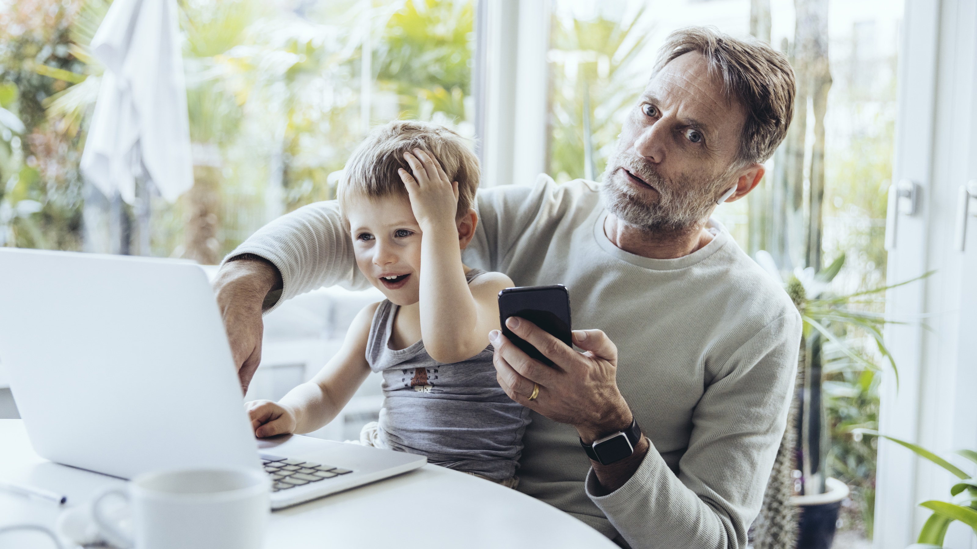 An older man looks like "uh oh" while his grandson sits on his lap with an "uh oh" hand to his head.