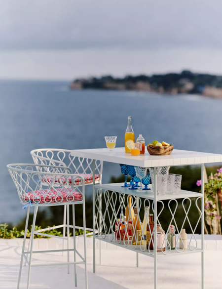 Whimsical, powdery blue South-of-France-style outdoor bar furniture styled beachside with patterned seat cushions and assorted bar accessories.