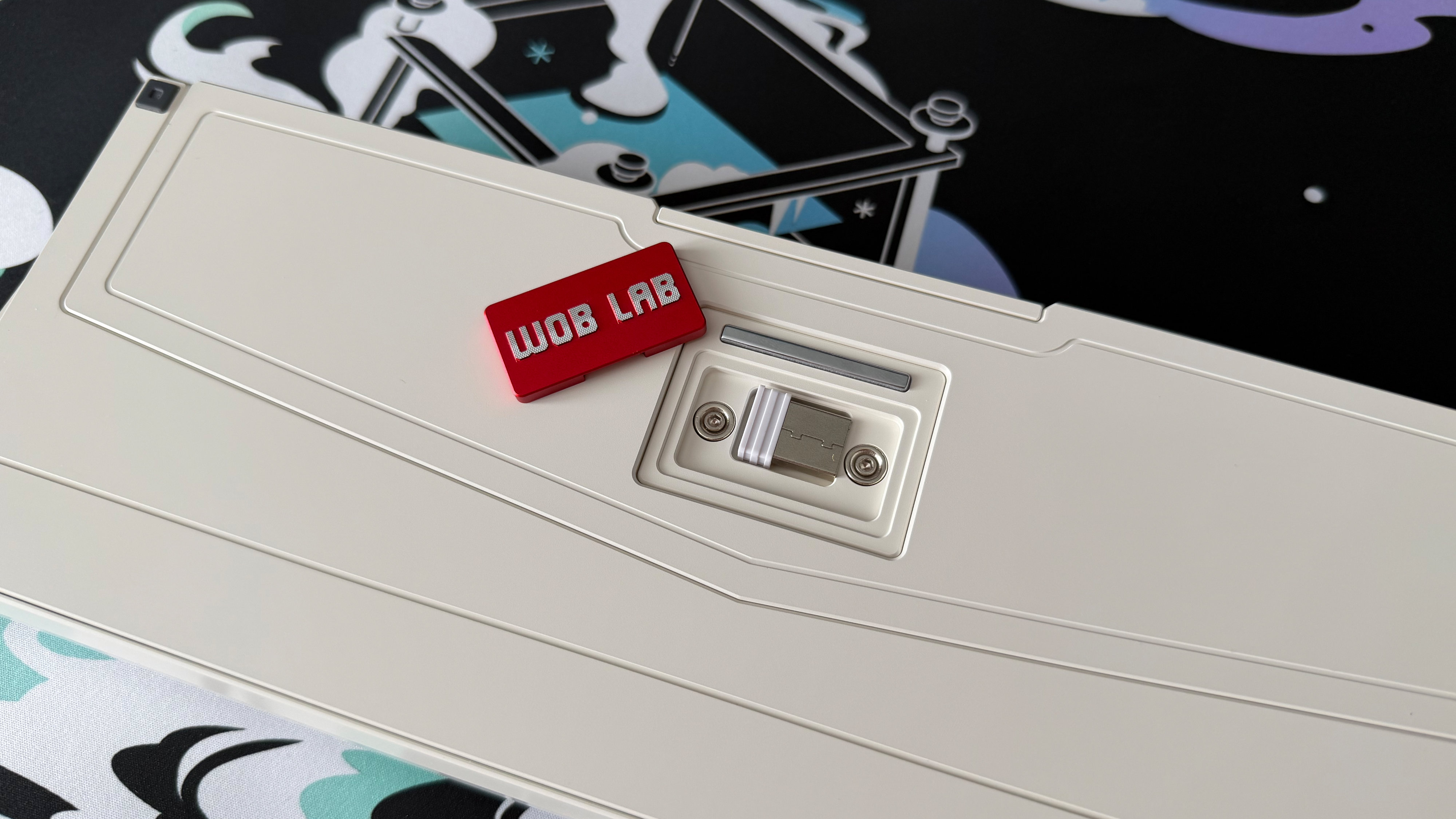 The underside of the Wobkey Zen 65 Ultra, showing its metal plate reading 'Wob Lab' and the compartment it usually hides containing its USB dongle.