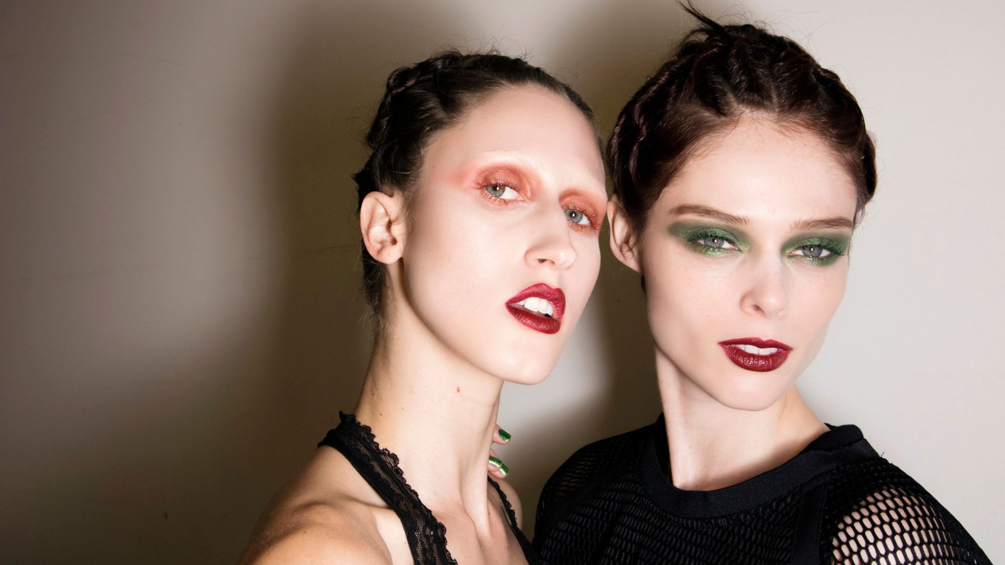 two models backstage wearing bright eyeshadow and dark red lipstick
