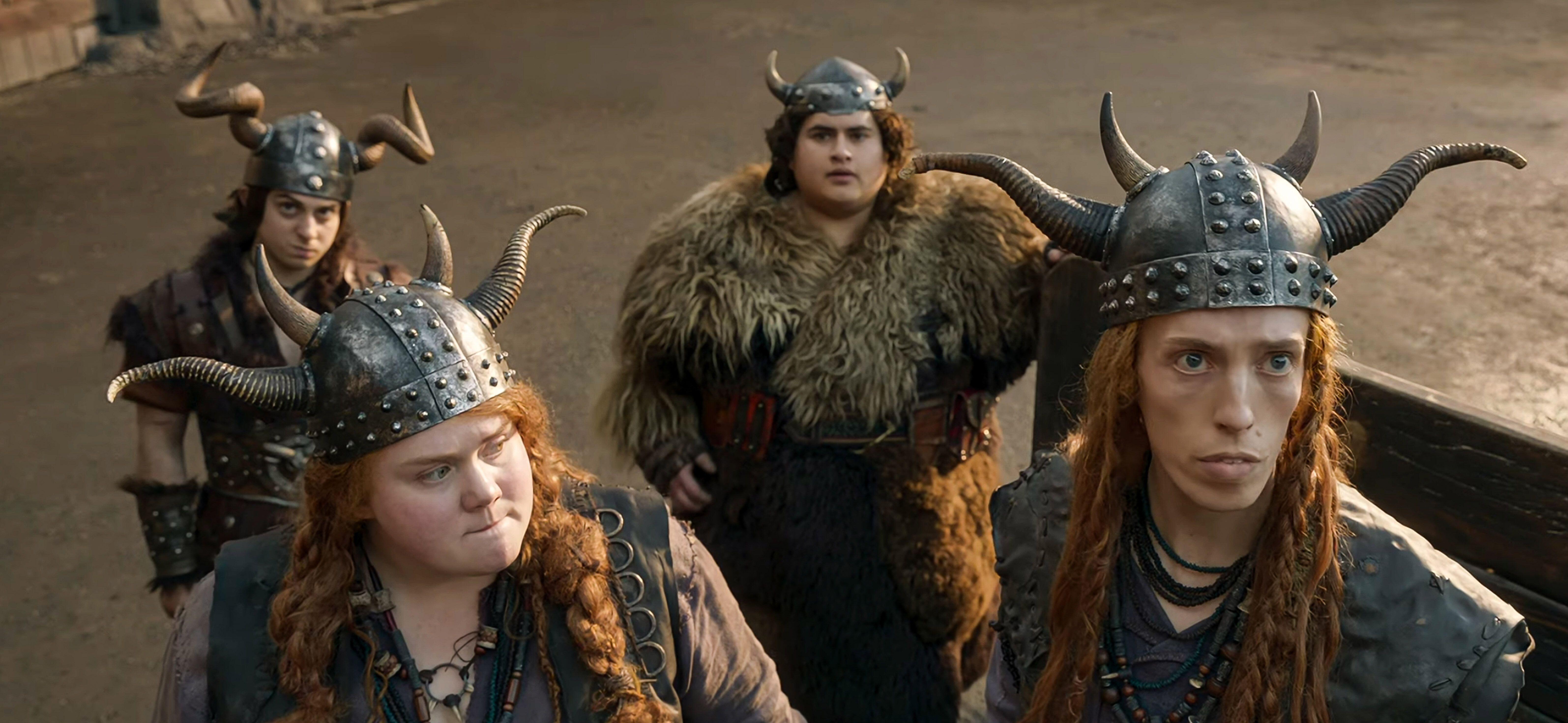 four characters (snotlout, fishlegs, ruffnut, tuffnut) from the live-action how to train your dragon 2025 remake, wearing viking helmets in a training arena