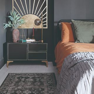 A dark grey-painted bedroom with a vintage-style runner rug by the side of the bed