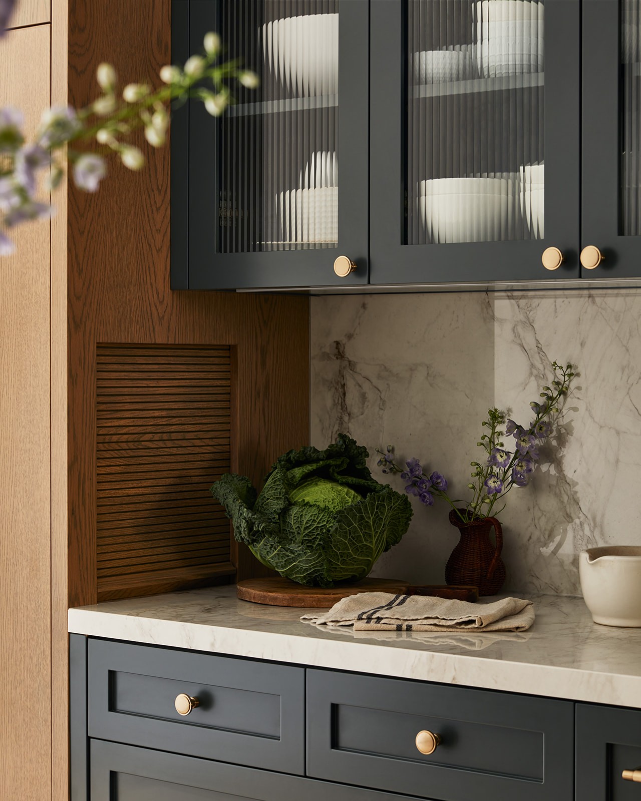 black kitchen cabinets with gold handles and marble backsplash next to a dark wood cabinet with small square wood garage door.