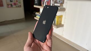 En hand håller upp en svart iPhone SE från 2022 i ett rum, med baksidan vänd mot kameran.