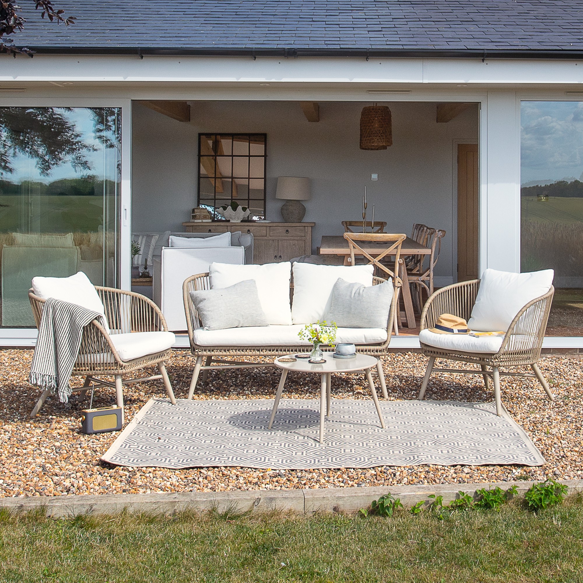 A garden with an outdoor lounging set with white cushions and a rope design on top of an outdoor rug