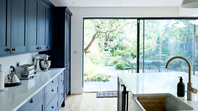 Contemporary blue kitchen with white acrylic worktops looking out through large sliding doors onto garden