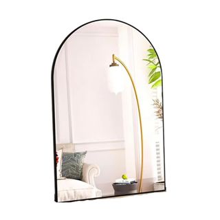 A black arched mirror reflecting a room with a lamp