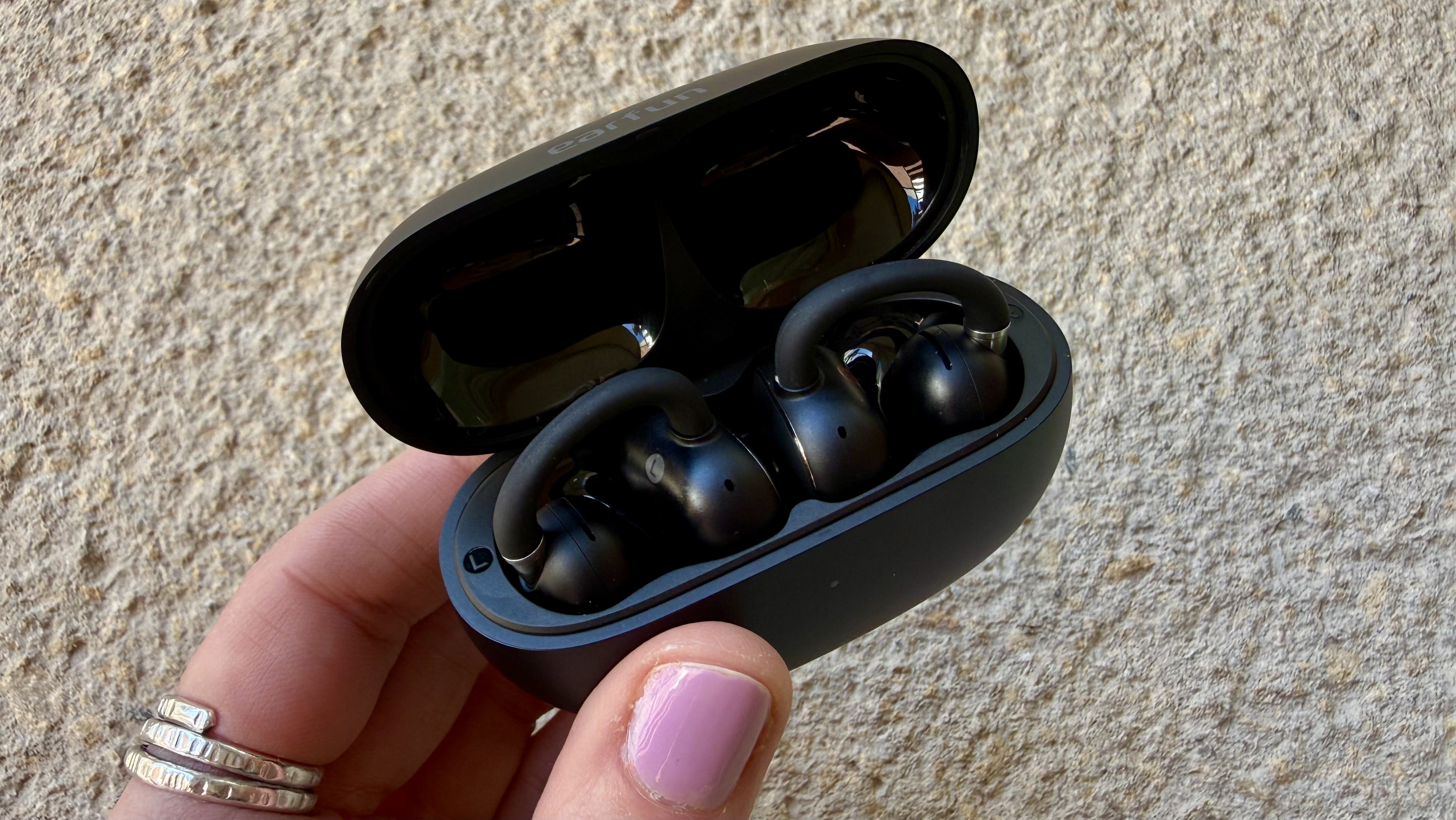 Someone holding the EarFun Clip 2 in their charging case
