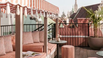 Flamingo pink cushioned terrace seating with a striped tassel-accent canopy and petite patio table