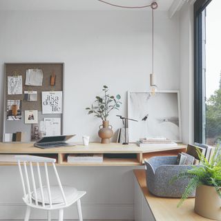 A bright white-painted home office with a large window and a pendant light hanging above the desk