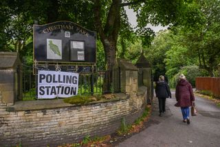 People walking into a park next to a big sign that says polling station