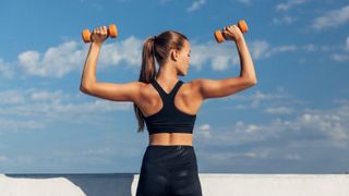 the back of a woman lifting light dumbbells in a shoulder press move