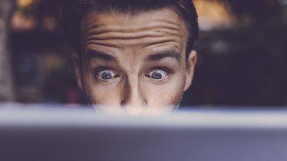 A shocked-looking man looks at his laptop screen.