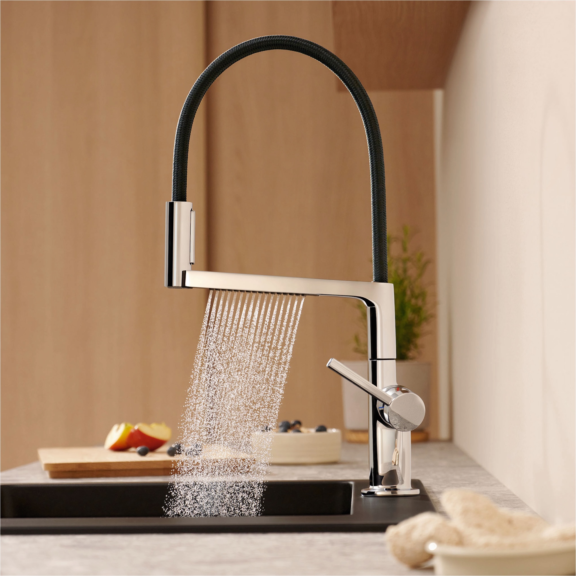 a modern kitchen tap in black and chrome showing an eco-friendly water spray with a chopping board with fruit on it next to the sink and a plant on the corner of the counter