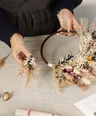 Hands attaching small bunches of dried flowers onto a wreath