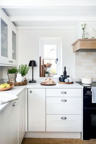 kitchen with white beams and quarry tiles with white cabinets and small window with black range cooker