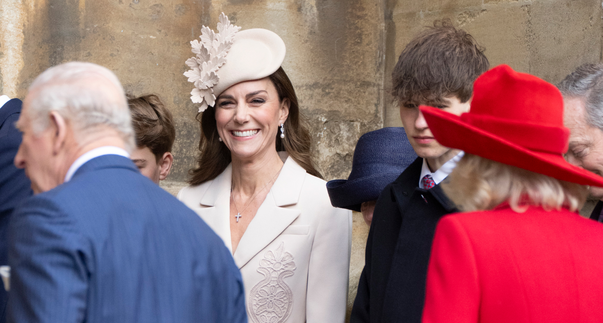 Princess Kate wearing a beige coat and hat and smiling behind The King and Queen