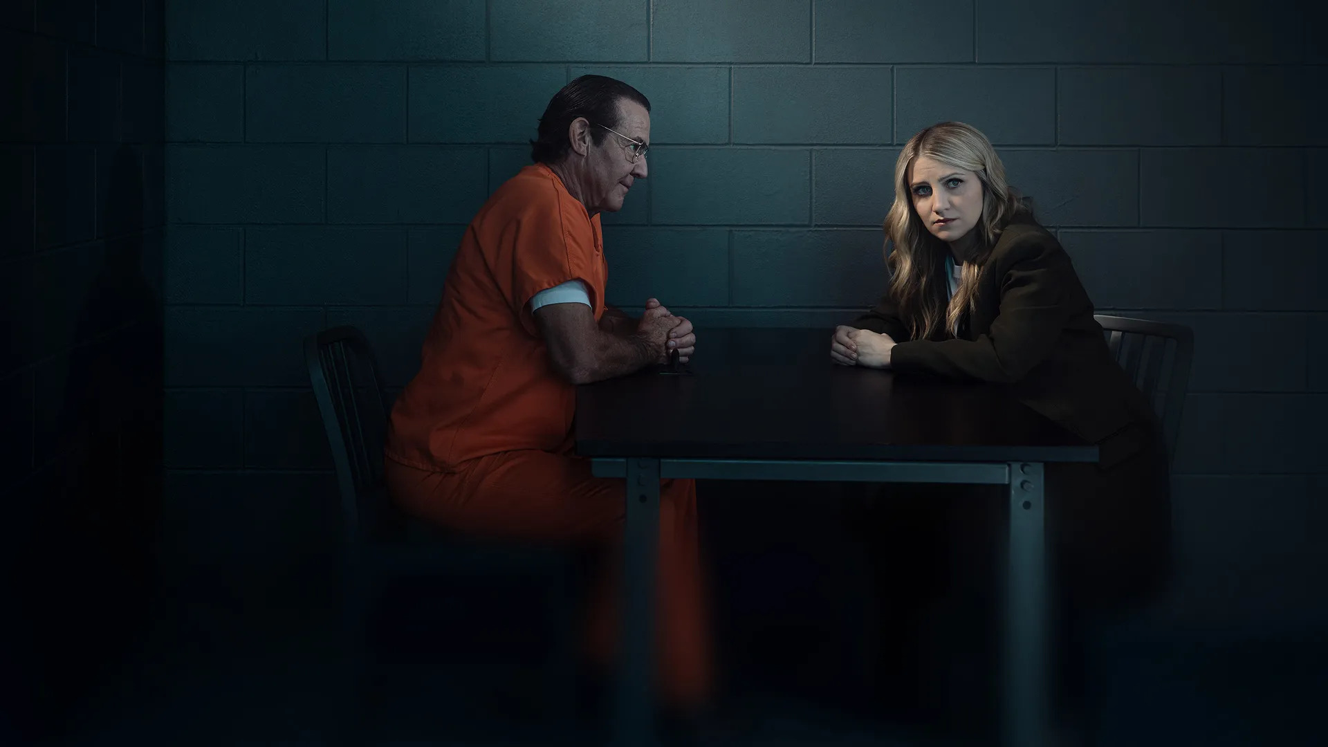 dennis quaid in an orange jump suit sitting across from annaleigh ashford as melissa moore in a jail in a promotional still for happy face