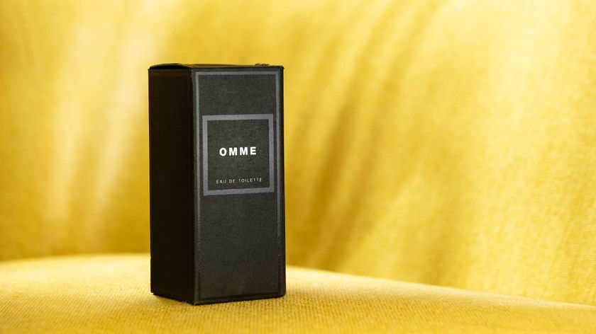 A sleek black box labeled &quot;OMME Eau de Toilette&quot; set against a soft yellow background