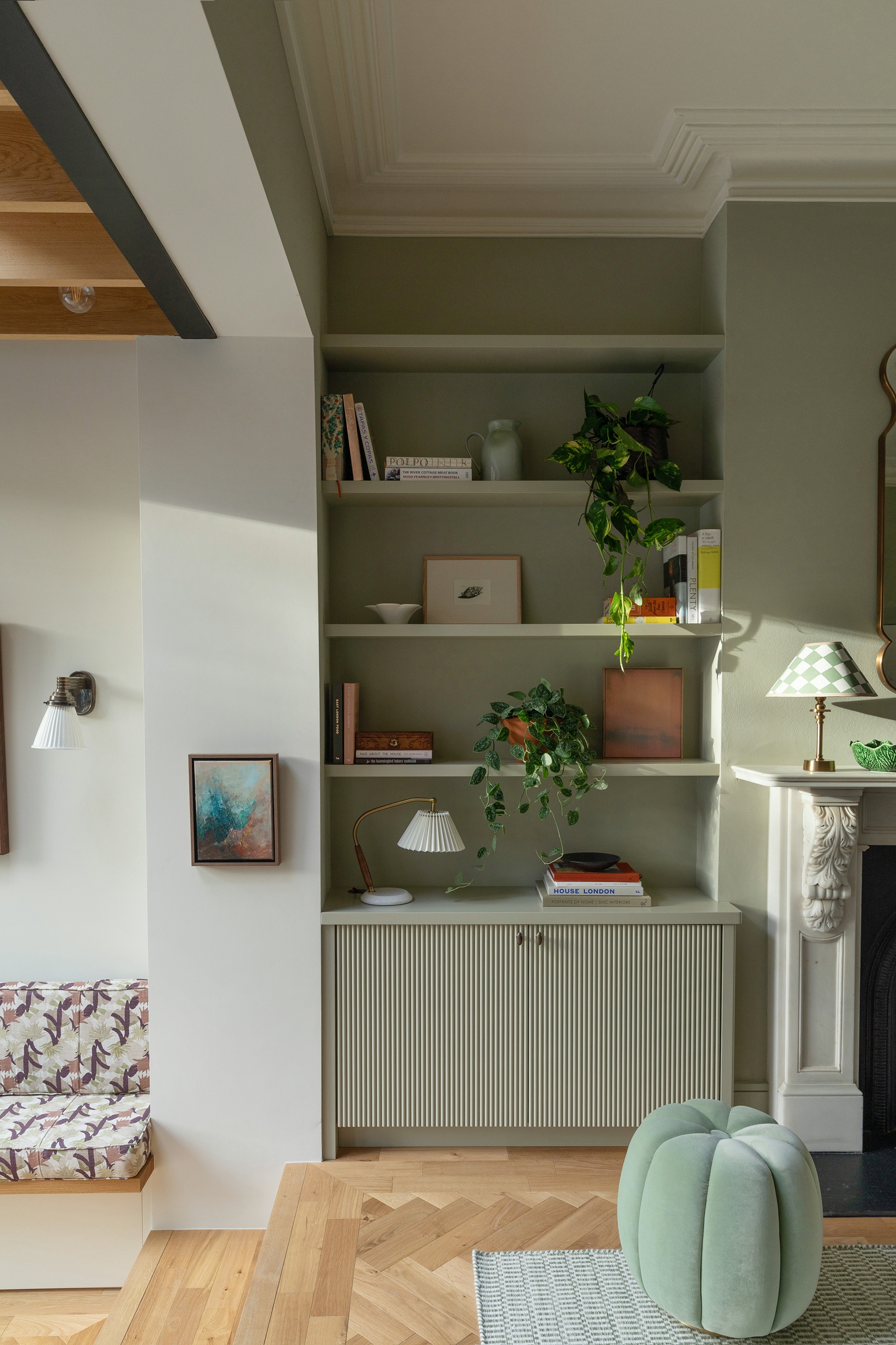 built-in shelves in living room painting in sage green with fluted cupboards, timber floors, the edge of a fireplace, steps down into another room with banquette seat