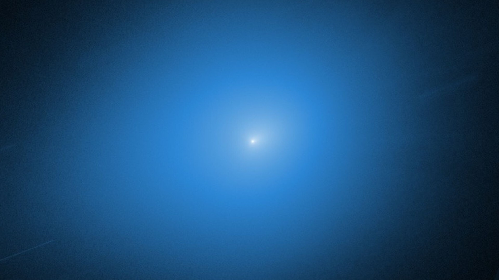 A white light of the comet 3I/ATLAS is surrounded by a blue glow against a black background