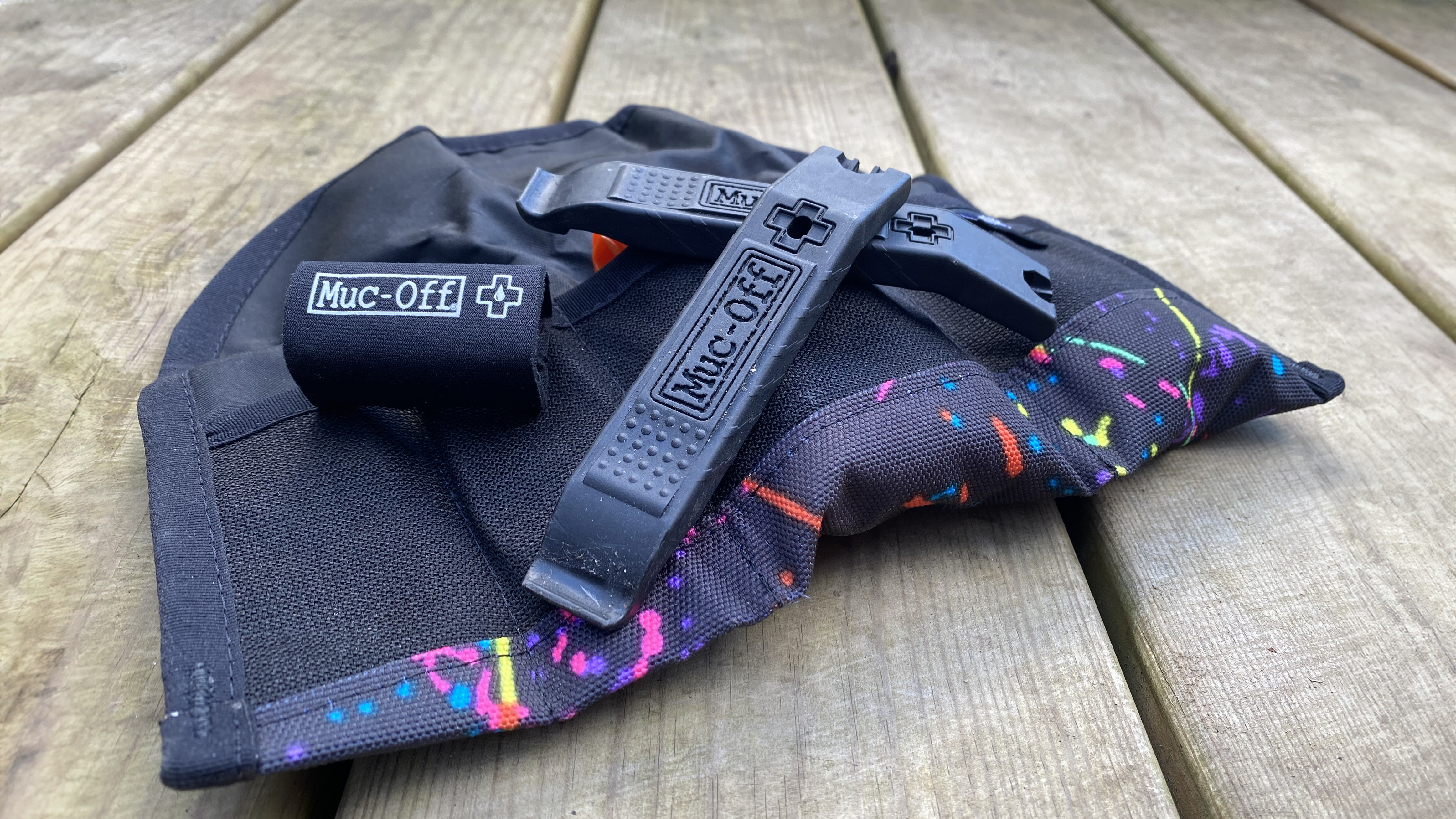 Black Muc-Off Rim Stix tyre levers one resting on top of the other against and placed on top of a Wizard Works tool wrap, on a wooden deck