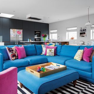 Open-plan living room and kitchen with bright blue sofas and ottoman and monochrome rug