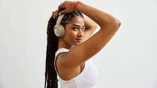 A young woman with black braided hair and a white vest top models a pair of JBL Tune 780NC headphones