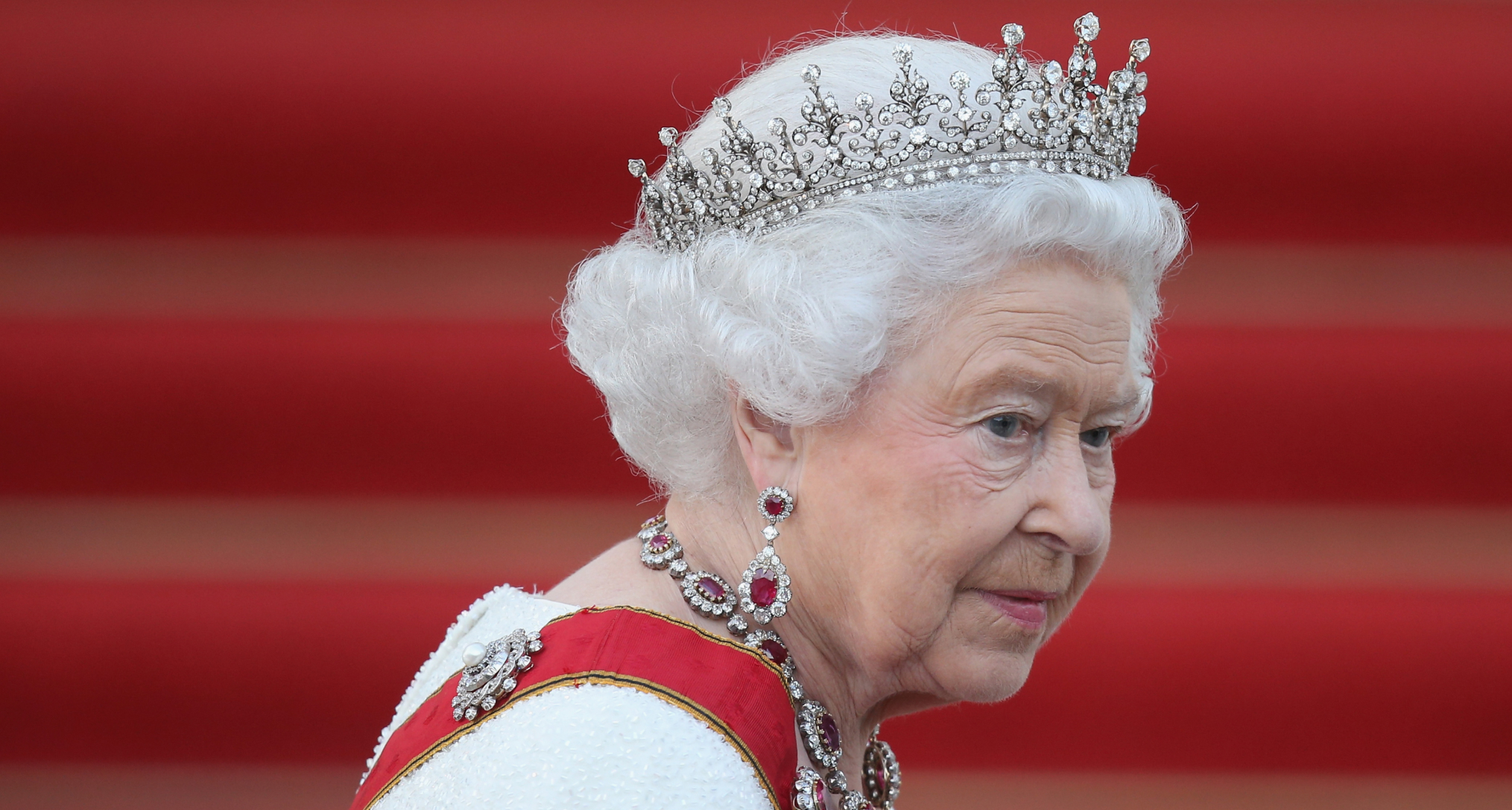 Queen Elizabeth wearing a white dress, red sash and tiara