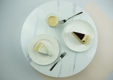 Two cake slices on white plates, with coffee in a glass. It's set on a marble table.