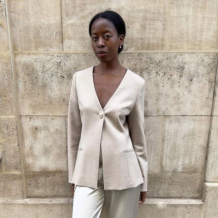 a woman wearing a cream button jacket, white pants, and black pointed toes
