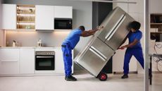 Two people wheeling a broken fridge out of a kitchen