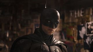 Robert Pattinson casts a sideways glance while standing in The Riddler's apartment in The Batman. 