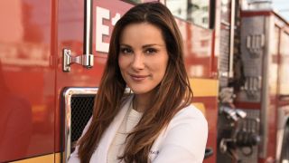 Stefania Spampinato stands with her arms crossed in front of a firetruck in an ABC press photo for Station 19 as Carina De Luca.