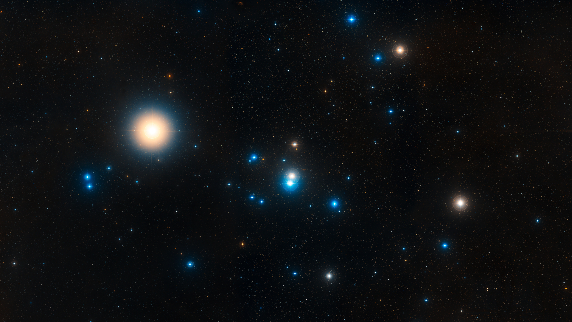 A collection of bright yellow and blue stars are arrayed in a sideways 'V' formation against a dark sky peppered with distant stellar bodies.