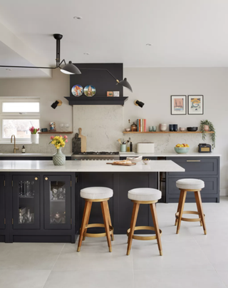 A black kitchen with white walls and floors, white wooden bar stools and kitchen island with glass panes