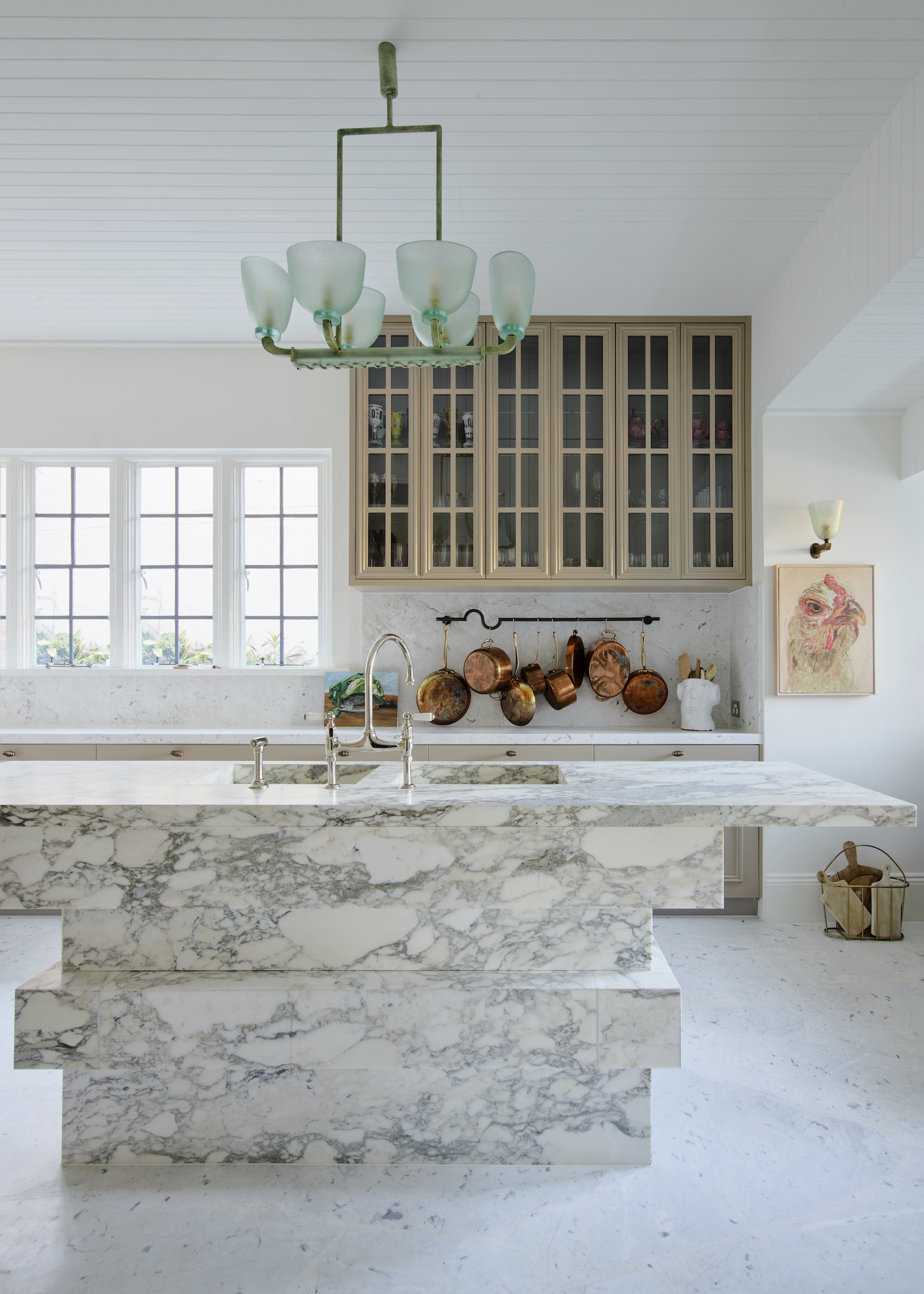 marble island with vintage chandelier hanging above the island. There is also a view of the glass fronted cabinets.