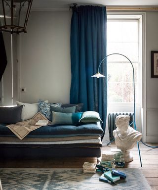 A classical inspired living room picture with blue drapes and marble bust.