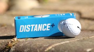 TaylorMade Distance+ Golf Ball resting on a wall along with its packaging
