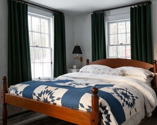 bedroom with wooden Shaker style bed, blue and white patterned throw, Gustavian nightstand and dark green curtains