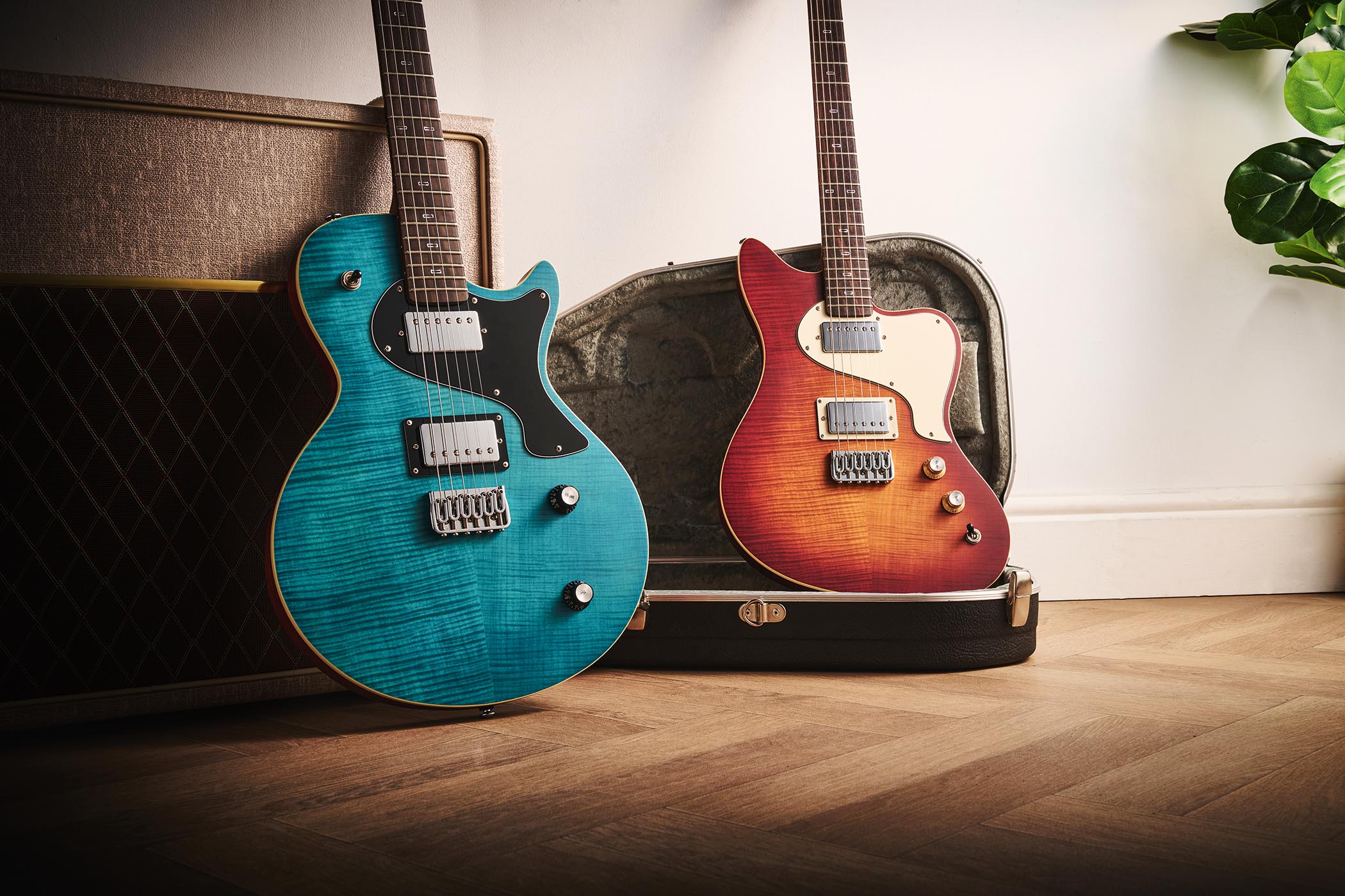 PJD Origin Series Carey Pro and PJD Origin Series St John Pro: the Sea Blue and Original Burst electric guitars are photographed against a fawn-coloured Vox amp with the offset resting on top of its case.