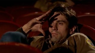Robert De Niro holding his fingers up to his face while sitting in a movie theater in Taxi Driver