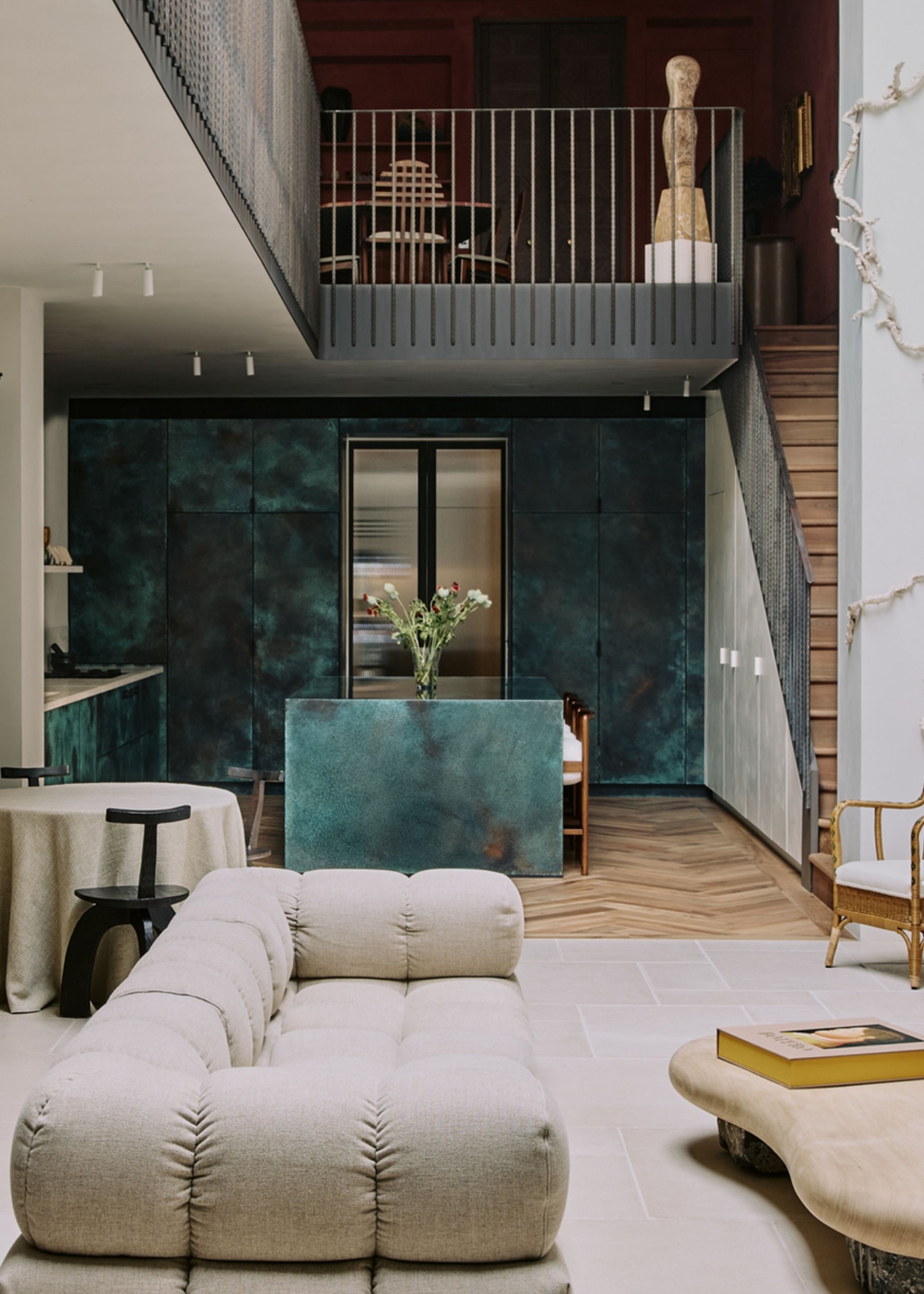 Image of a kitchen in the back of an open plan living room with a loft above it. The kitchen has exposed copper panelling across the cabinetry.