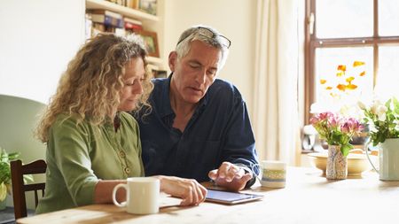 An older couple looks thoughtful while sitting at a table together and looking at a tablet.