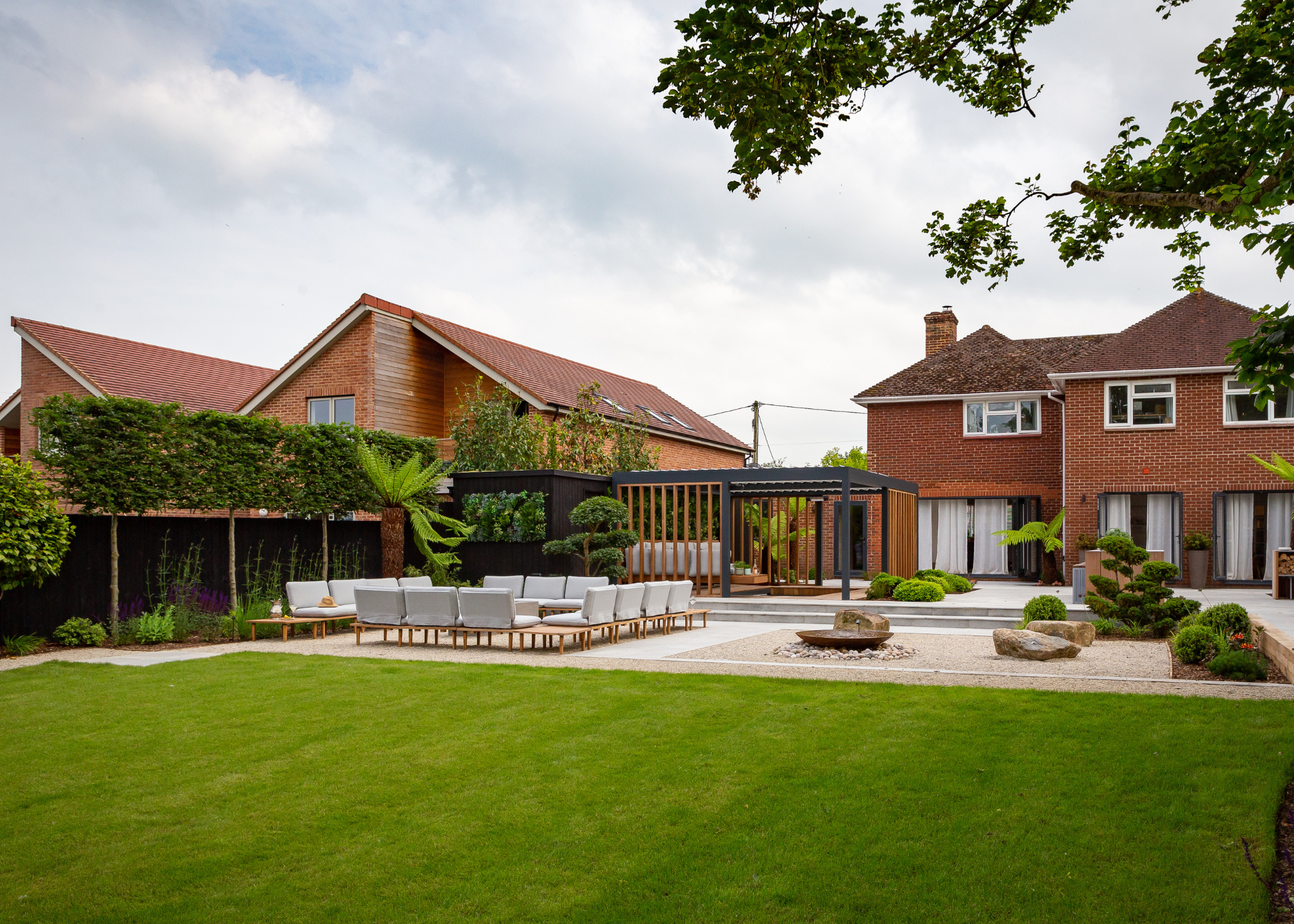 an expansive garden with bright green lawns, and a paved seating area with a pergola at the back