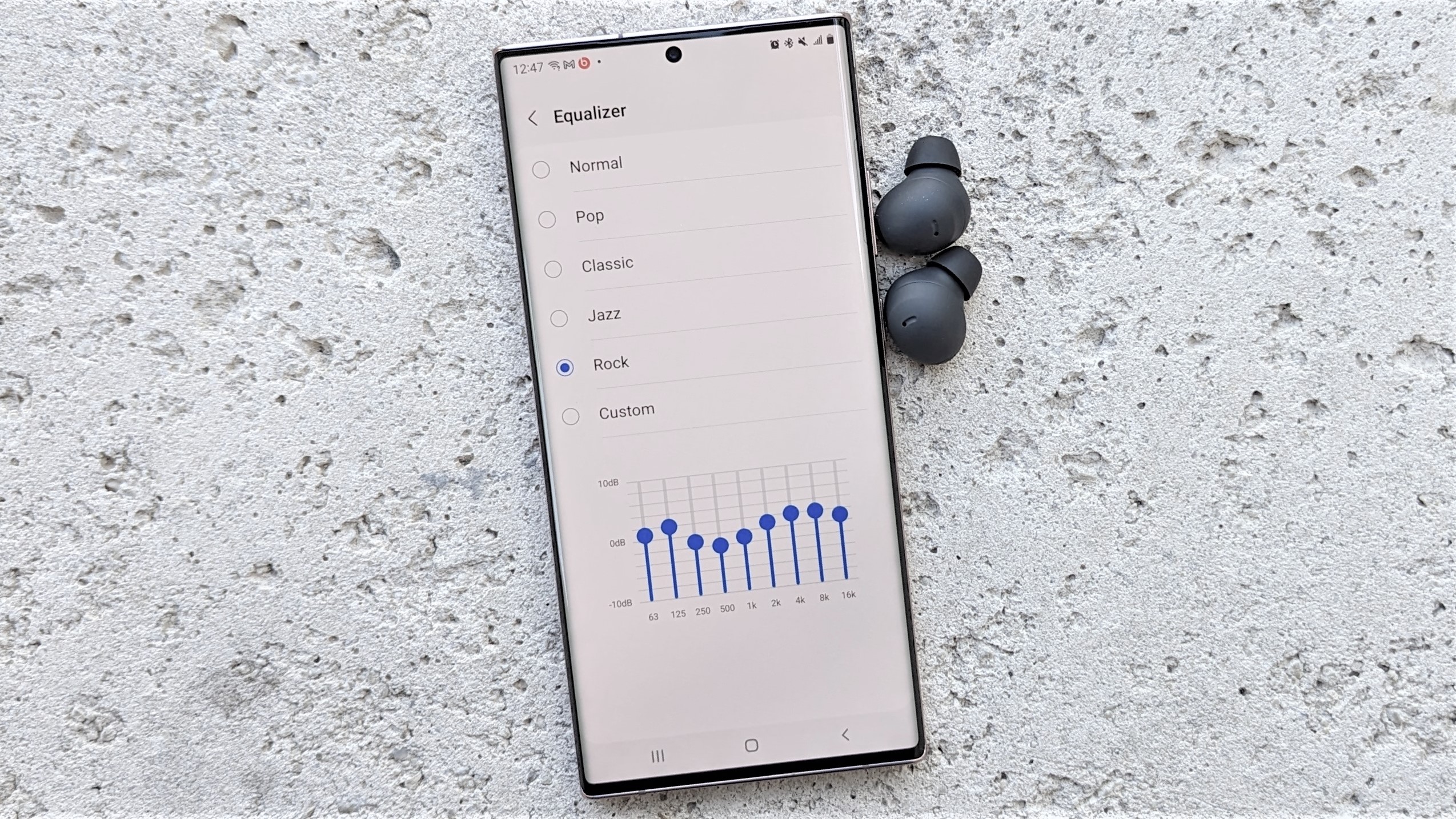 Смартфон Samsung Galaxy с наушниками, помещенными на каменную поверхность, с настройками настройки эквалайзера