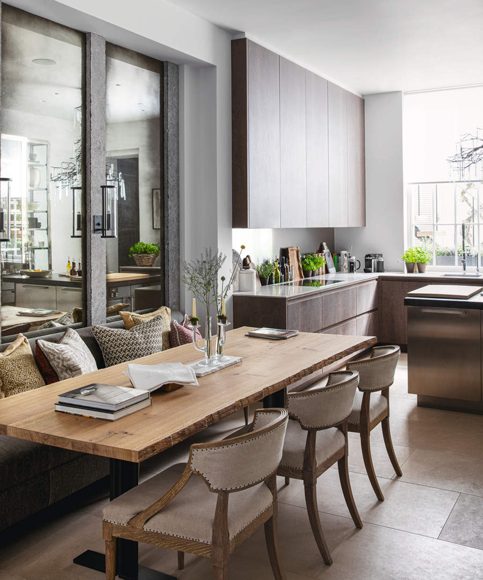 Dining area with long wooden table in a kitchen diner, grey kitchen cabinets and tiled flooring. A renovated four storey London townhouse, home of Louise Bradley, interior designer.