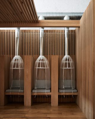 Hair drying pods at Spiral (x,y,z) featuring vertical wood slats, dryers and seats with grey cushions