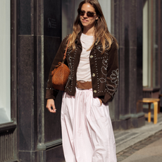 Fashion person Rosie Huntington-Whiteley wears the pale pink trouser trend. She pairs her trousers with a white tank top, khaki raffia tote and thong sandals on holiday. She is looking down, holding her son's head in front of a old-fashioned ice-cream shop in a recent image from her Instagram.