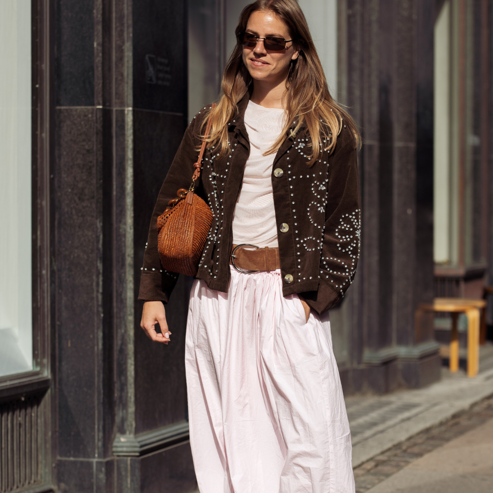 Fashion person Rosie Huntington-Whiteley wears the pale pink trouser trend. She pairs her trousers with a white tank top, khaki raffia tote and thong sandals on holiday. She is looking down, holding her son's head in front of a old-fashioned ice-cream shop in a recent image from her Instagram. 